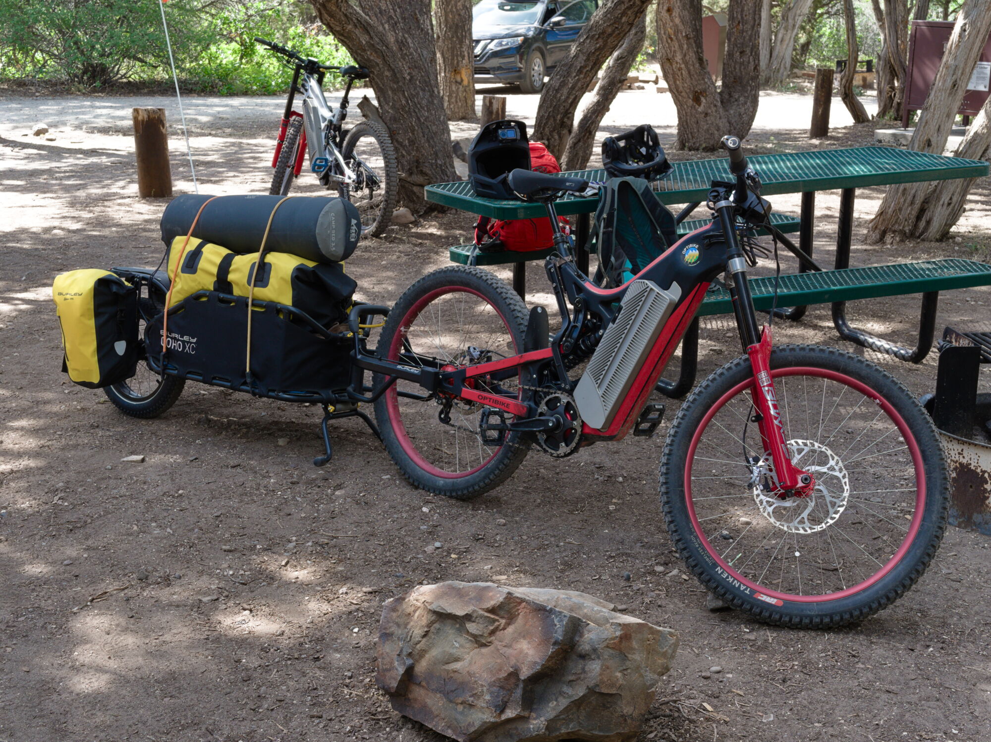 Optibike R22 Everest, 300 mile range ebike parked at a campground with a large trailer attached to it full of camping gear.