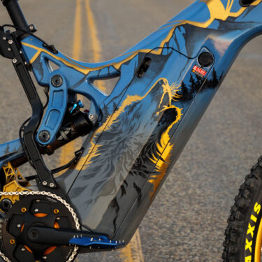 A close up of the painted frame on an Optibike E-Bike, showing the hand painted wolf howling at the sky, painted in vibrant gold color.