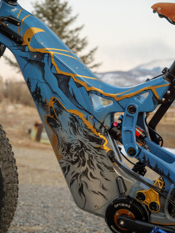 A close up of the painted frame on an Optibike E-Bike, showing the hand painted wolf howling at the sky, painted in vibrant gold color.