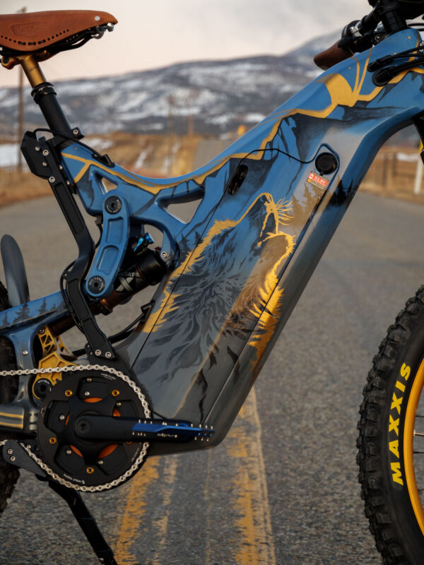 A close up of the painted frame on an Optibike E-Bike, showing the hand painted wolf howling at the sky, painted in vibrant gold color.