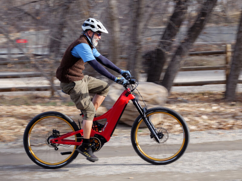 Rider testing the high-speed capability of the Optibike Altus electric mountain bike on a trail, demonstrating stable handling at speed with motion blur.